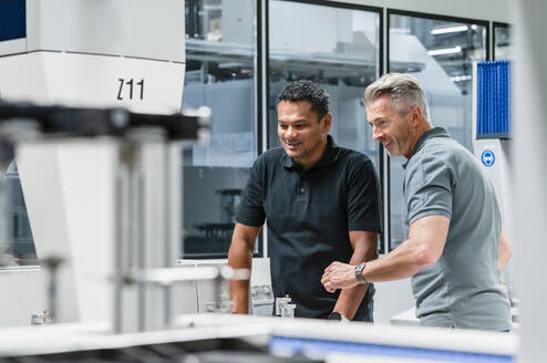 Lächelnde Ingenieure, die über automatisierte Maschinen in einer Fabrik diskutieren - DIGF17056