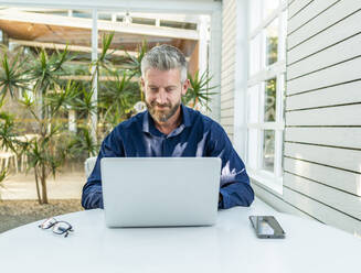 Male entrepreneur teleworking with a netbook at table with smartphone in outdoor cafe - ADSF32456