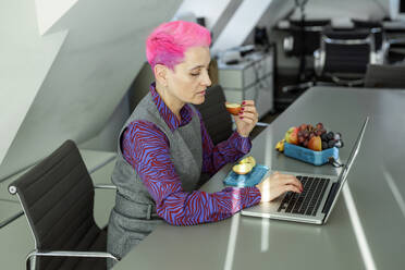 Geschäftsfrau isst Apfel mit Laptop am Schreibtisch im Büro - AANF00250