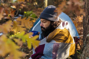 Bärtiger Mann trinkt Kaffee im Becher im Herbstwald - MRRF01743