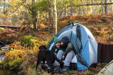Mann küsst Freundin mit Hund im Zelt im Herbstwald - MRRF01744