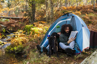 Hipster-Mann liest Buch mit Freundin und Hund im Zelt im Wald - MRRF01745