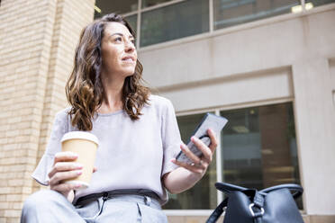 Nachdenkliche Geschäftsfrau mit Einwegbecher und Mobiltelefon - WPEF05590