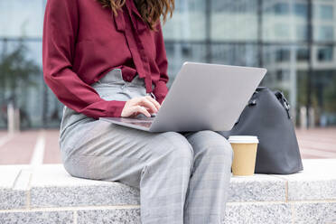 Businesswoman using laptop sitting on bench at office park - WPEF05605