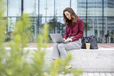 Businesswoman using laptop on bench at office park - WPEF05609