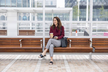 Businesswoman with disposable cup sitting on bench at railroad station - WPEF05614