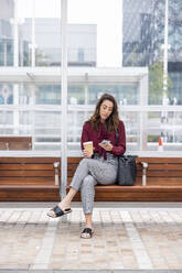 Businesswoman with disposable cup using smart phone waiting at railroad platform - WPEF05615
