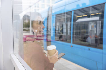 Geschäftsfrau mit Einwegbecher durch Glas gesehen beim Warten am Bahnhof - WPEF05616