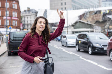 Geschäftsfrau mit erhobener Hand ruft ein Taxi auf einer Straße in der Stadt - WPEF05622