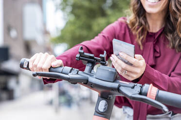 Businesswoman using mobile phone to unlock electric bicycle in city - WPEF05627