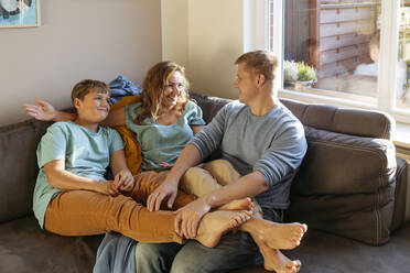 Smiling woman talking with man and son on sofa at home - IHF00691