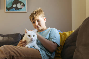 Niedlicher Junge streichelt Katze auf Sofa zu Hause - IHF00692