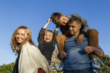 Happy parents carrying playful sons on sunny day - IHF00699