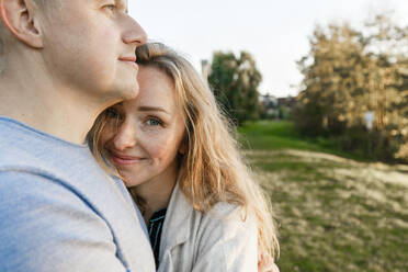 Blond woman embracing boyfriend in park - IHF00713