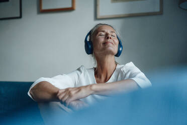 Lächelnde Frau, die zu Hause über Kopfhörer Musik hört - JOSEF06098