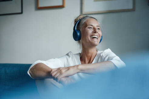 Happy woman listening music through headphones at home - JOSEF06099