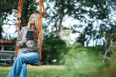 Woman holding tablet PC on swing at backyard - JOSEF06107