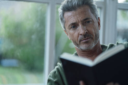 Mann, der vor einem Fenster ein Buch liest - JOSEF06128