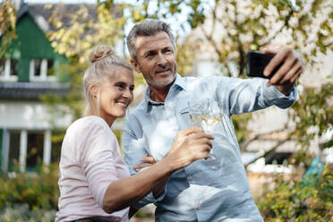 Smiling man taking selfie with woman through mobile phone at backyard - JOSEF06150