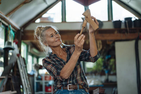 Woman holding wooden tool at garden shed - JOSEF06153