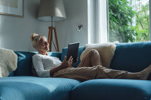 Frau mit Tablet-PC entspannt sich auf dem Sofa zu Hause - JOSEF06160