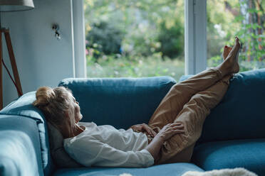 Frau entspannt sich mit hochgelegten Füßen auf dem Sofa zu Hause - JOSEF06165