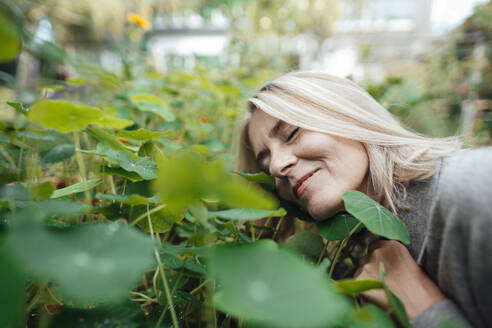 Lächelnde blonde Frau riecht an Pflanzen im Garten - JOSEF06169