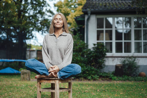 Woman practicing yoga on stool at backyard - JOSEF06176