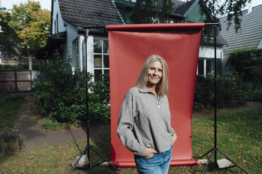 Smiling woman with hands in pockets at backyard - JOSEF06185