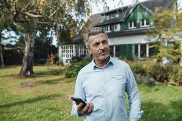 Mann hält Smartphone im Hinterhof - JOSEF06188