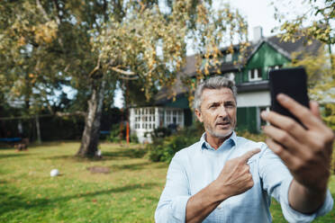 Man attending video call through mobile phone at backyard - JOSEF06192