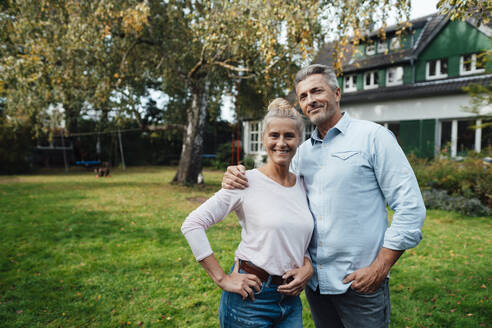 Smiling man standing with arm around woman at backyard - JOSEF06198