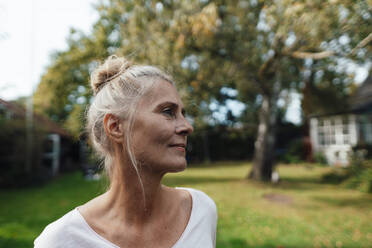 Thoughtful woman with hair bun at backyard - JOSEF06199