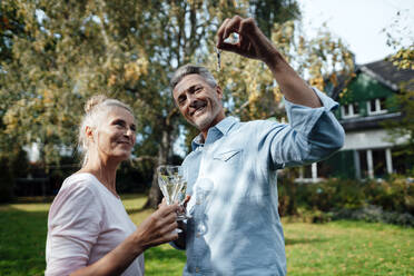 Smiling man holding champagne flute and house key by woman at backyard - JOSEF06207