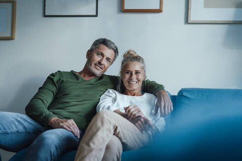 Smiling man with arm around woman's shoulder on sofa - JOSEF06230
