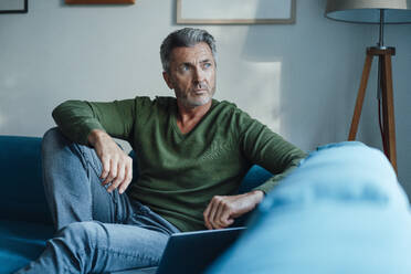 Man sitting by laptop on sofa at home - JOSEF06234