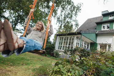 Playful woman swinging on swing at backyard - JOSEF06242