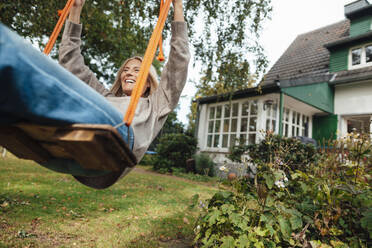 Happy woman swinging on swing at backyard - JOSEF06243