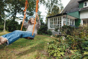 Woman swinging on play equipment at backyard - JOSEF06244