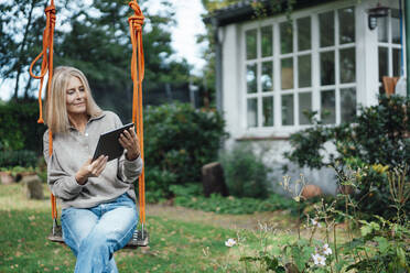 Woman using tablet PC on swing at backyard - JOSEF06250