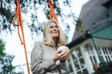 Frau hält Kaffeetasse auf Schaukel im Hinterhof - JOSEF06252