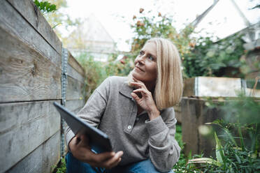 Blond woman with hand on chin holding tablet PC at garden - JOSEF06260