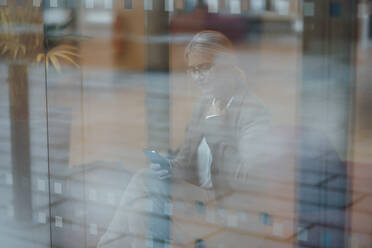 Geschäftsfrau benutzt Mobiltelefon hinter Bürofenster - JOSEF06263