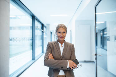 Businesswoman with arms crossed at office corridor - JOSEF06267
