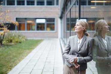 Businesswoman with mobile phone leaning on glass wall - JOSEF06272