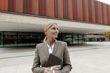 Blond businesswoman holding tablet PC on footpath - JOSEF06305
