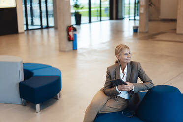 Lächelnde Geschäftsfrau mit Tablet-PC in der Büro-Lobby sitzend - JOSEF06321