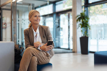 Geschäftsfrau sitzt mit Smartphone in der Büro-Lobby - JOSEF06331