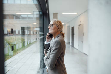 Businesswoman talking on mobile phone at office corridor - JOSEF06349