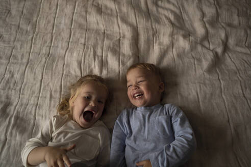 Unbekümmerte Zwillinge lachen zusammen auf dem Bett liegend zu Hause - SSGF00355